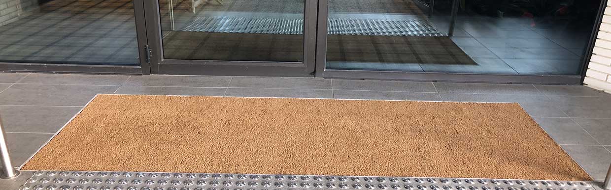 Top view of eco-friendly coir mats placed outside a modern UK home, with sunlight and wet footprints showing durability
